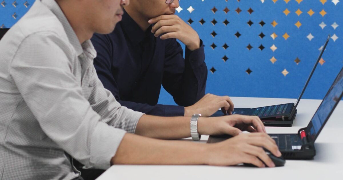 デスクでノートPCを囲んで書類を確認する2人